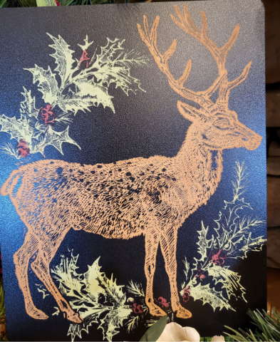 Brown reindeer and green and red holly painted on a black chalkboard. 